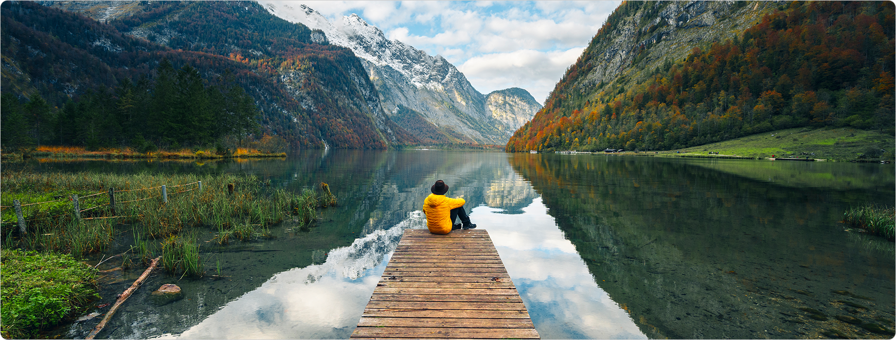 Image of man sitting at edge of a dock enjoying the moutain scenery